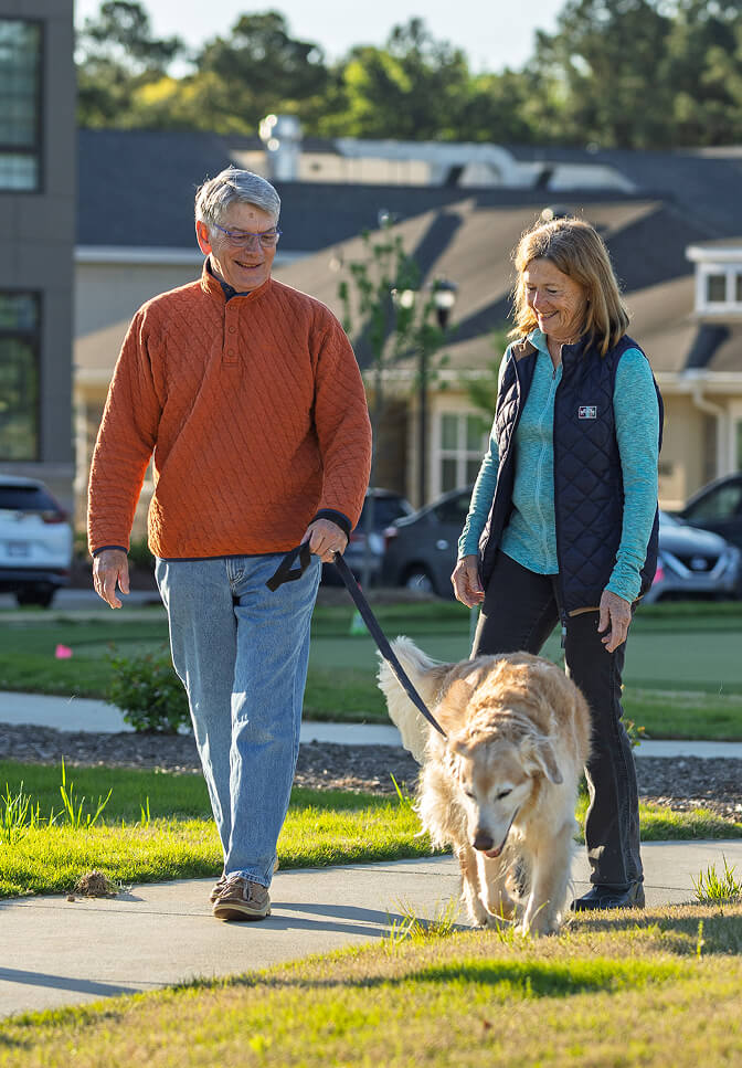 Senior Couple Walking Their Dog Outside Of Searstone Retirement Community